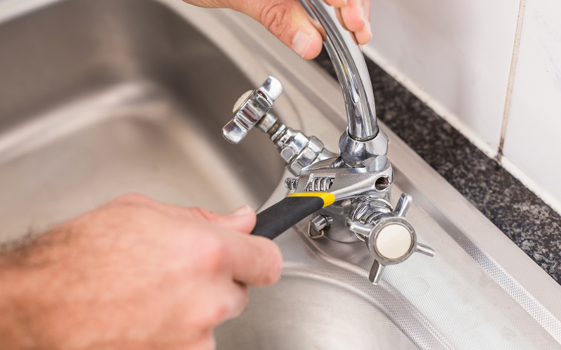 Hands using a wrench to repair a leaking sink tap.