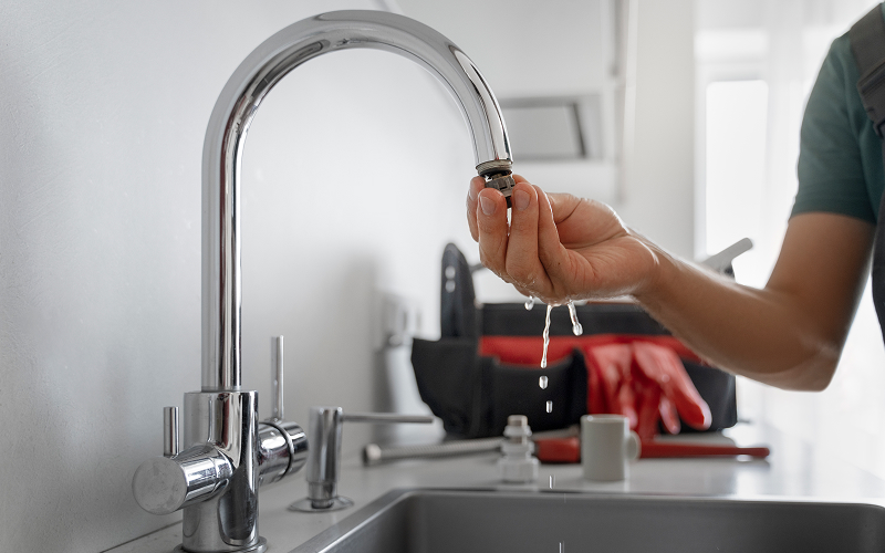 Plumber inspecting a dripping kitchen faucet to fix a leak.