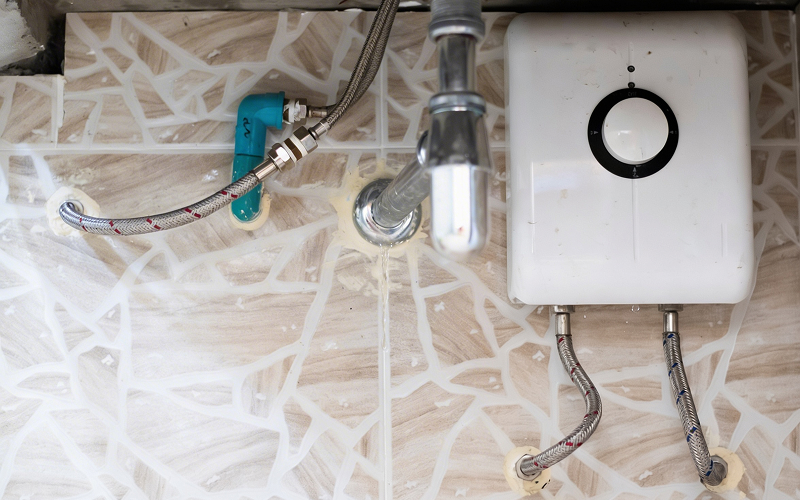 Water heater leaking from pipe connections on a tiled wall.