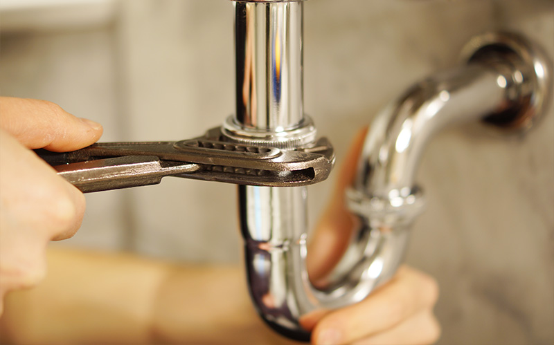 A person using a wrench to loosen the slip nuts of a P-trap under a sink