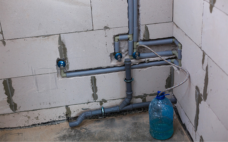 Exposed plumbing pipes with water container.