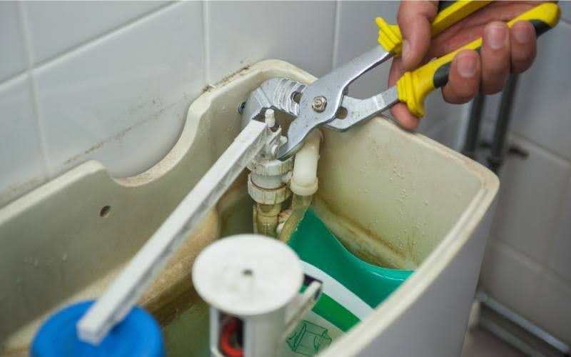 Hand repairing toilet tank mechanism.
