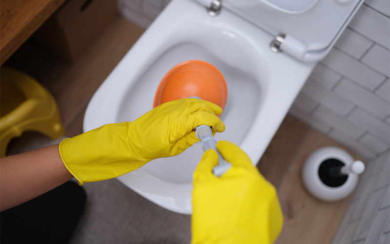 Person plunging toilet with rubber gloves.