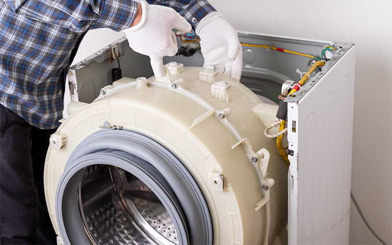 Person repairing front‑loading washing machine interior.