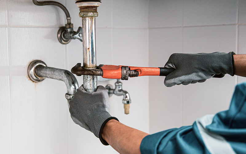Plumber using a pipe wrench to fix under-sink plumbing.