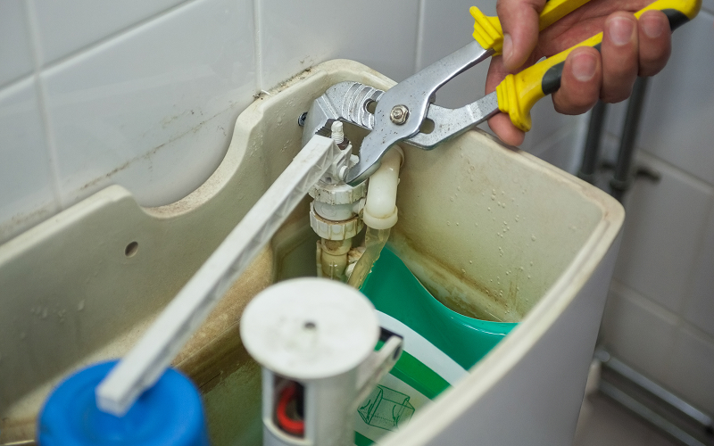 Plumber using pliers to repair loose toilet tank components.