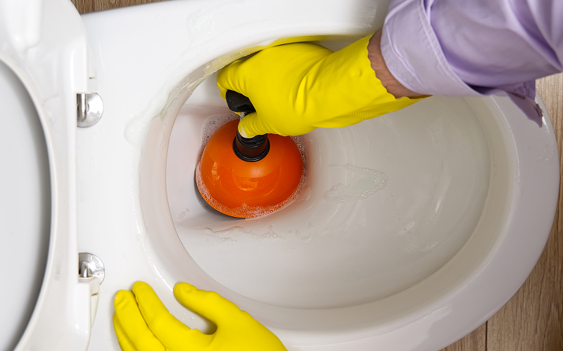 Unclogging a toilet bowl with a plunger for drainage.