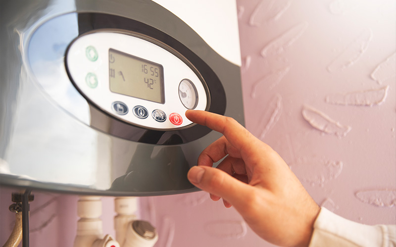 Hand adjusting settings on a digital water heater panel.